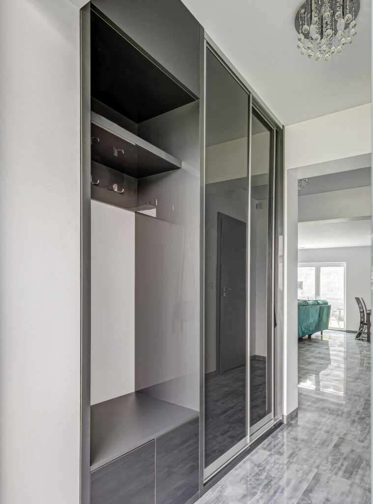 Wnętrze przedpokoju z lustrzaną szafą, szarymi płytkami i widokiem na jasny salon z oknami.