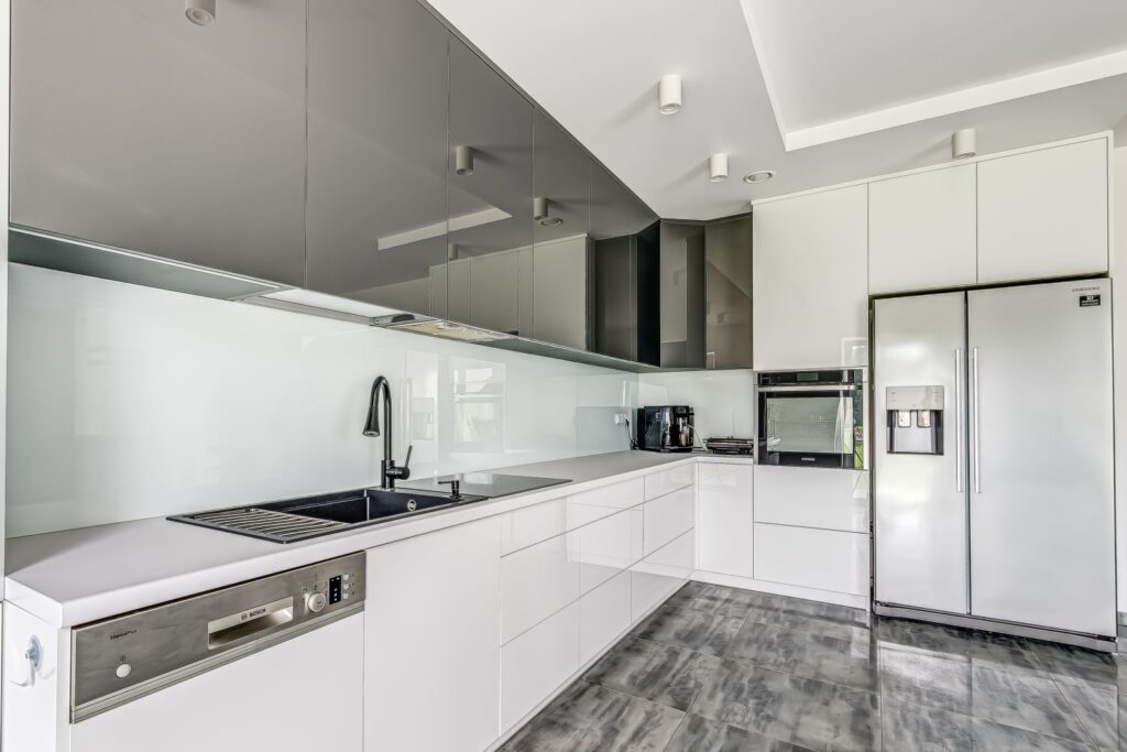 Nowoczesna kuchnia z białymi szafkami, zlewem, piekarnikiem, lodówką i pływającymi półkami w szarych odcieniach.