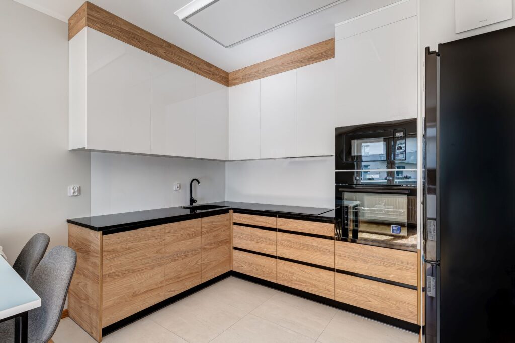 Nowoczesna kuchnia z jasnymi szafkami i drewnianymi frontami, czarnym blatem i lustrem w piekarniku.