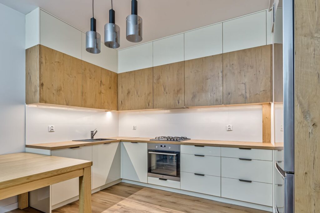 Nowoczesna kuchnia w kształcie litery L z drewnianymi i białymi szafkami, płyta gazowa i piekarnik.