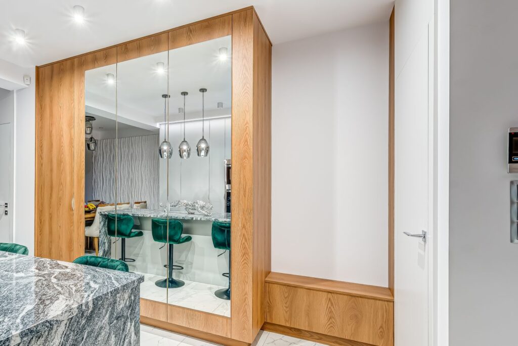 Nowoczesne wnętrze z drewnianymi szafkami i lustrzaną zabudową, marmurowy stół i zielone krzesła barowe.