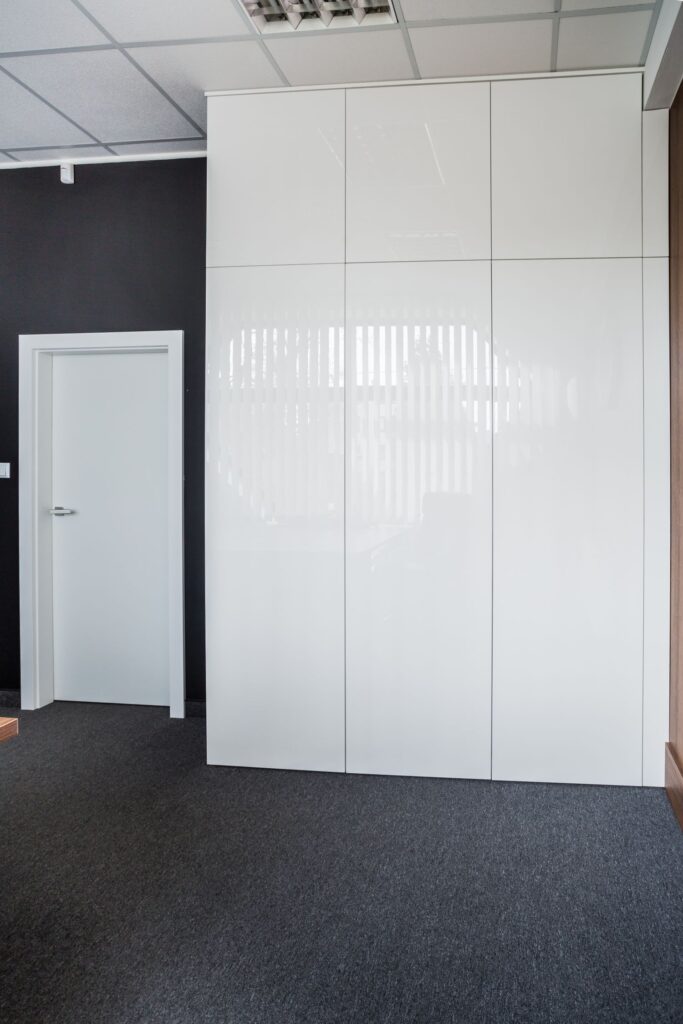 Biały minimalistyczny pokój z drzwiami i jasnym, błyszczącym regałem sięgającym sufitu.