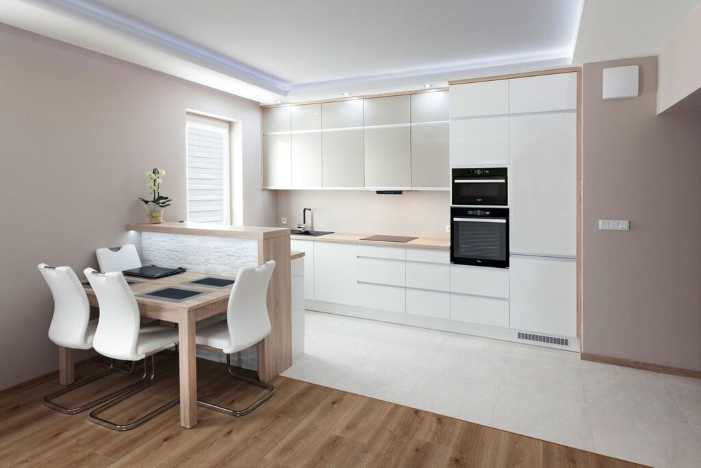 Nowoczesna kuchnia z białymi szafkami, drewnianym blatem, stołem i krzesłami. Minimalistyczny design i jasne wnętrze.