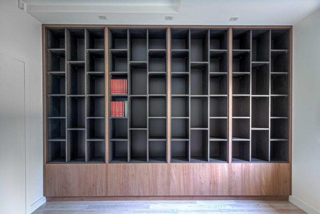 Pusta biblioteczka z ciemnego drewna z kilkoma czerwonymi książkami pośrodku półek.