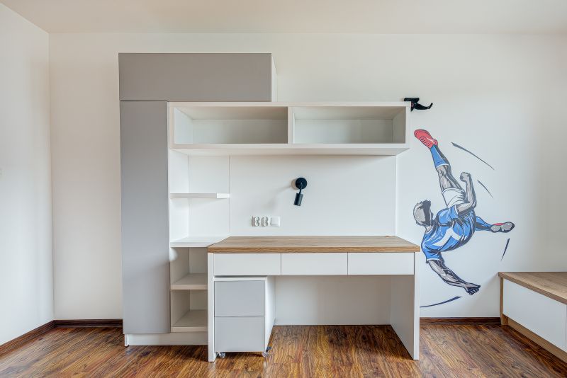 Biurko z jasnym blatem, nad nim półki oraz grafika piłkarza na ścianie. Podłoga drewniana.