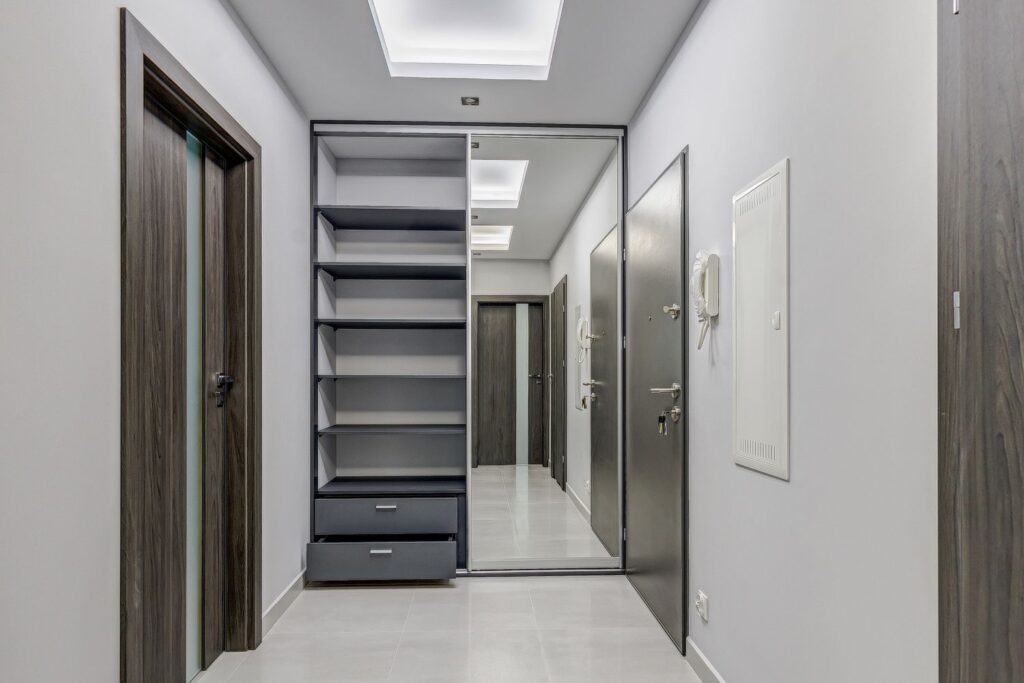 Nowoczesny, minimalistyczny korytarz z półkami, lustrem i drzwiami w ciemnym drewnie, oświetlony od góry.