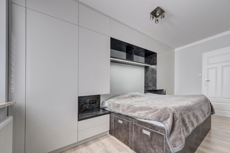 Nowoczesna sypialnia z dużym łóżkiem, zabudowanymi szafami i eleganckim oświetleniem, utrzymana w jasnych, stonowanych kolorach.