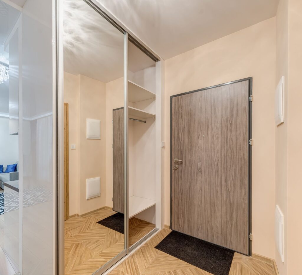 Nowoczesny przedpokój z lustrem przesuwnym, drewnianymi drzwiami i jasną, drewnianą podłogą.