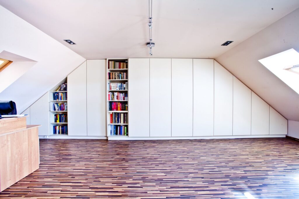 Nowoczesne poddasze z białymi szafami, regałami na książki i drewnianą podłogą.