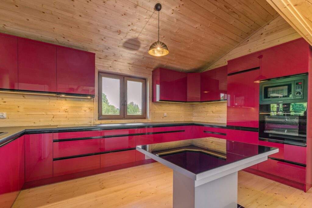 Nowoczesna kuchnia z czerwonymi szafkami, drewnianymi ścianami i sufitem, oraz dużym oknem i wyspą kuchenną.