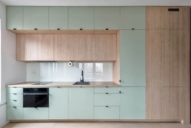 Nowoczesna kuchnia z miętowymi i drewnianymi szafkami, czarnym piekarnikiem i zlewem, minimalistyczny design.