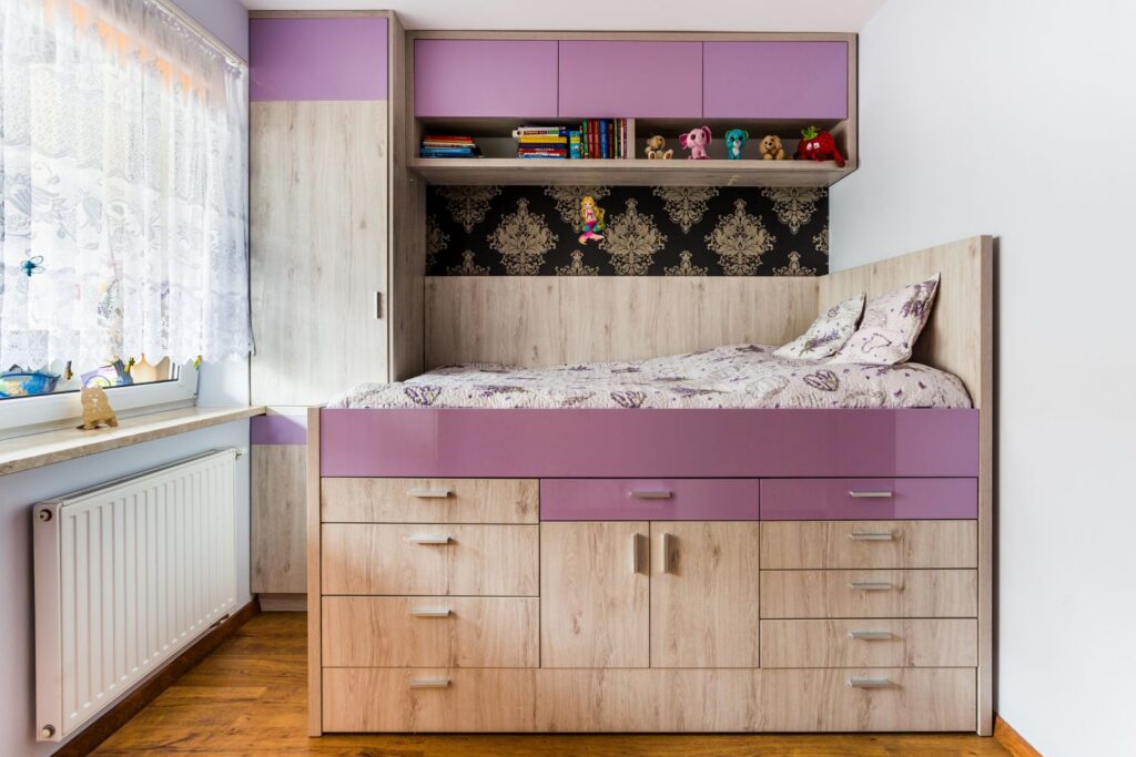 Łóżko piętrowe z fioletowymi i drewnianymi akcentami, z półkami, szufladami i dekoracjami dziecięcymi.