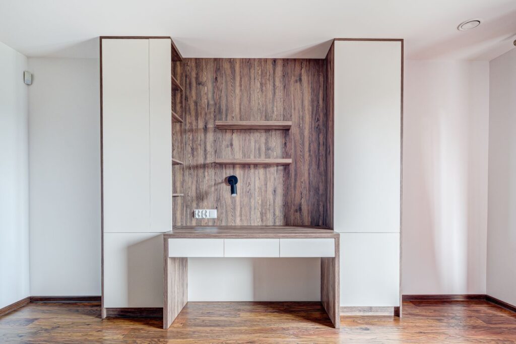 Drewniane biurko z białymi szufladami, półkami i zabudową, na tle drewnianej ściany w nowoczesnym pomieszczeniu.