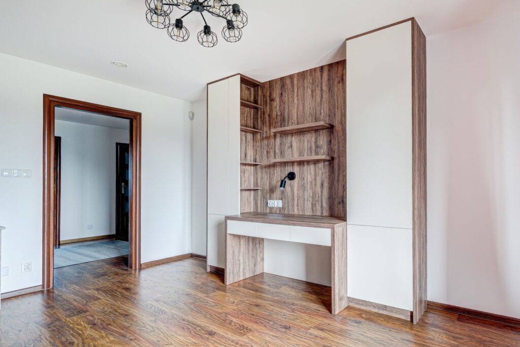 Nowoczesne biurko z drewnianymi półkami w jasnym pokoju, na tle białej ściany. Stylowy żyrandol u góry.