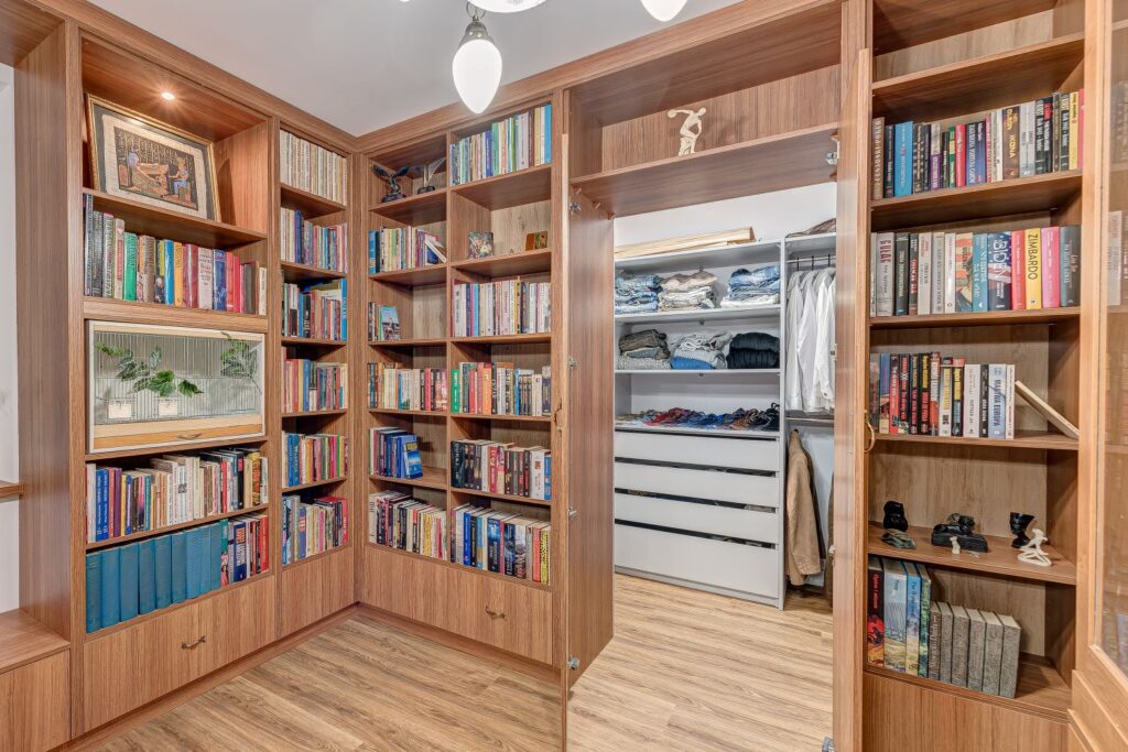Biblioteczka z drewnianymi półkami pełna książek w eleganckim gabinecie z przyległą garderobą.