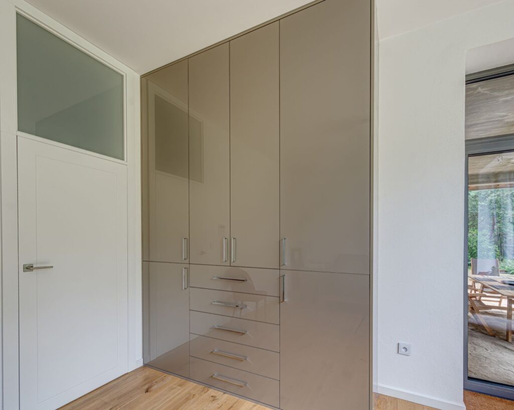 Szafa z wysokim połyskiem i szufladami w nowoczesnym pomieszczeniu z drewnianą podłogą.