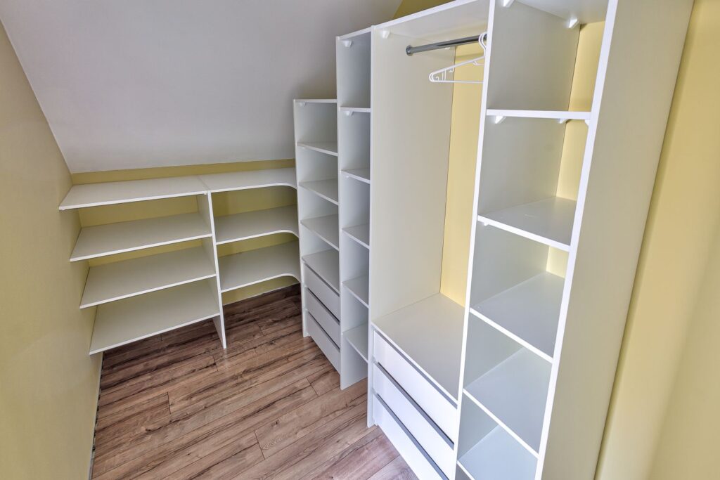 Biała, nowoczesna garderoba z półkami i wieszakami, żółte ściany, drewniana podłoga.