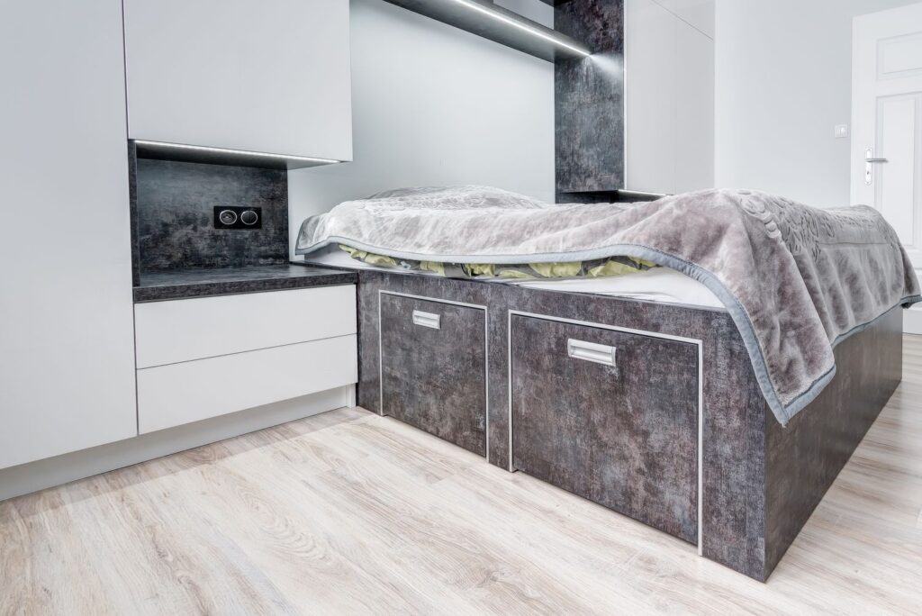 Nowoczesna sypialnia z drewnianą podłogą, zabudowanym łóżkiem i białymi szafkami, oświetlenie LED.