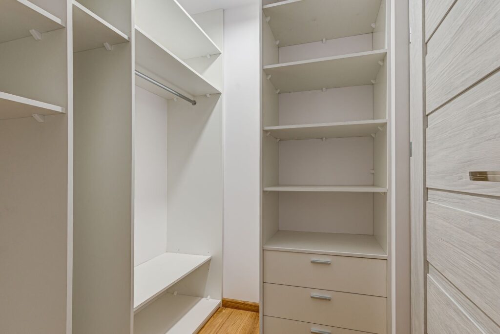 Szafa wnękowa z białymi półkami i szufladami, pusta i gotowa na przechowywanie, w jasnym pokoju z drewnianą podłogą.